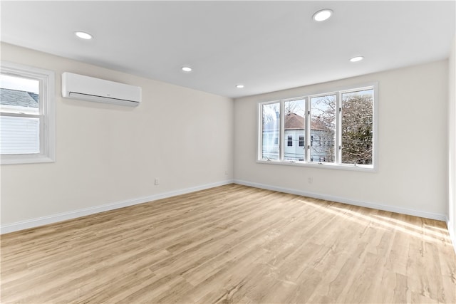 empty room featuring a wall mounted air conditioner, baseboards, light wood-type flooring, and plenty of natural light