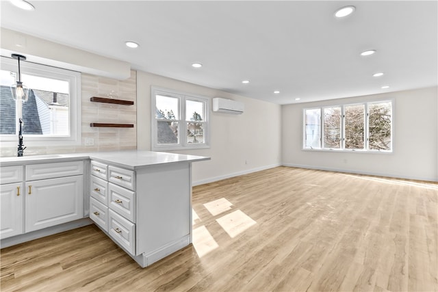kitchen with a sink, a wall unit AC, a peninsula, light wood-type flooring, and white cabinets