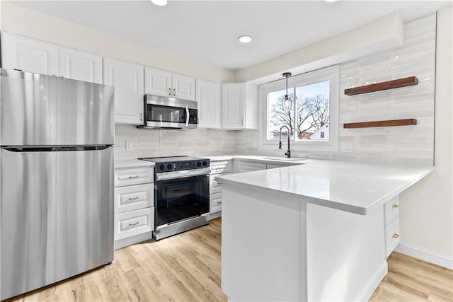 kitchen featuring white cabinets, light countertops, appliances with stainless steel finishes, and a peninsula