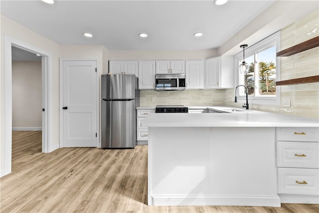 kitchen with light countertops, a sink, appliances with stainless steel finishes, a peninsula, and white cabinets