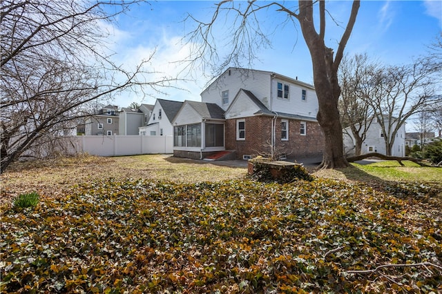 back of house with brick siding, a sunroom, and fence