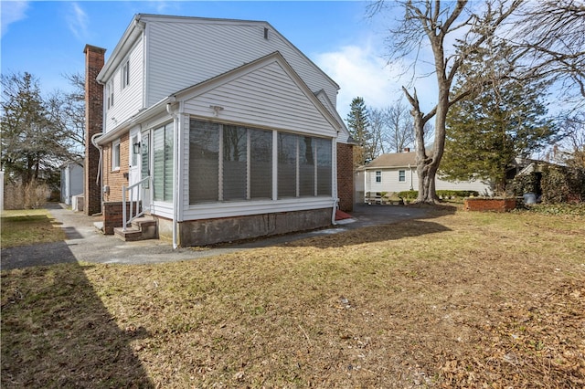 back of property featuring a chimney, a sunroom, a yard, and entry steps
