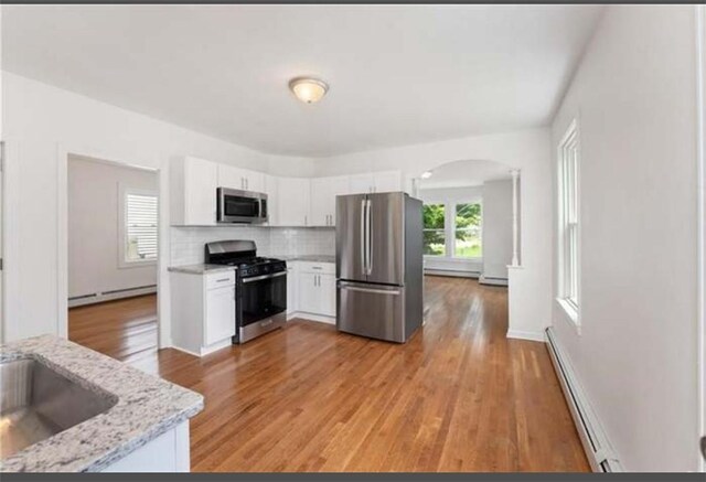 57 School St, East Providence, RI 02914 - kitchen with backsplash, arched walkways, a baseboard radiator, white cabinets, and appliances with stainless steel finishes