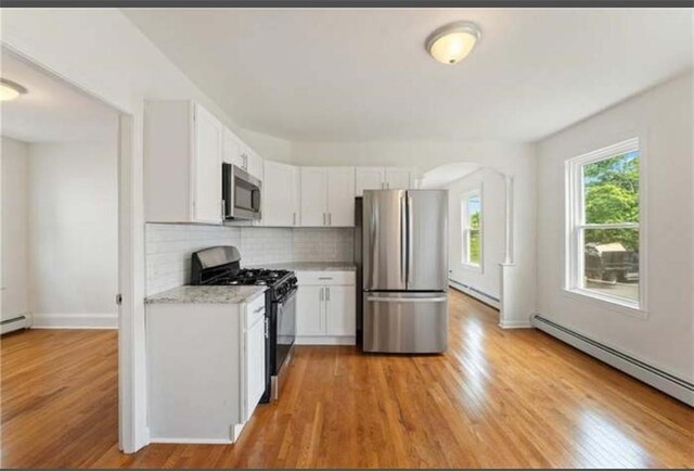 57 School St, East Providence, RI 02914 - kitchen with light countertops, stainless steel appliances, decorative backsplash, a baseboard radiator, and light wood-style flooring
