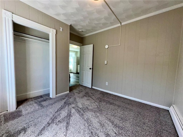 unfurnished bedroom with a baseboard heating unit, ornamental molding, carpet, baseboards, and a closet