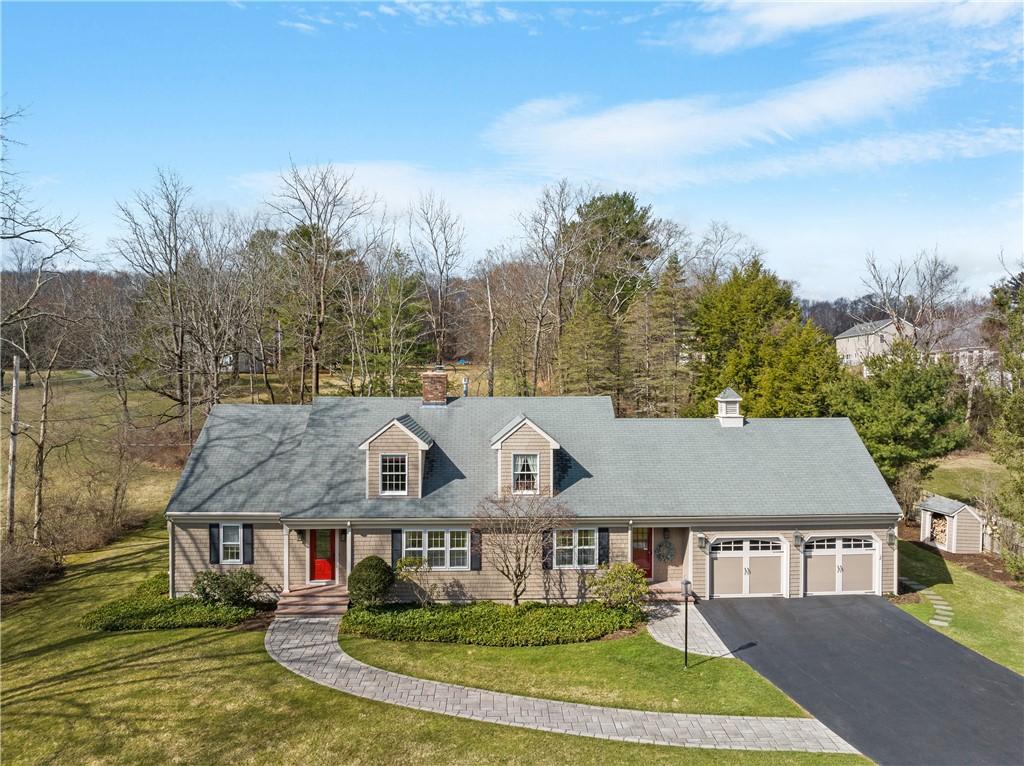 new england style home with aphalt driveway, an attached garage, a chimney, and a front lawn