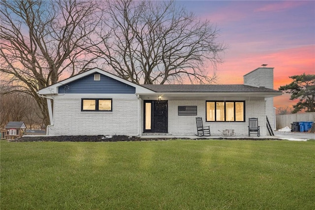view of front of house with a lawn, a chimney, fence, and brick siding