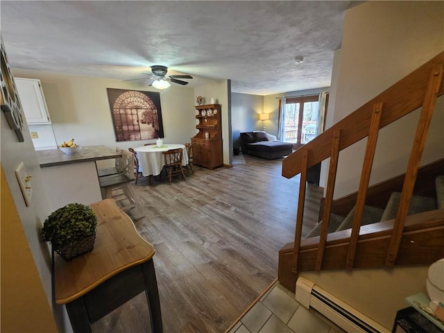 living area featuring a ceiling fan, a baseboard heating unit, and wood finished floors