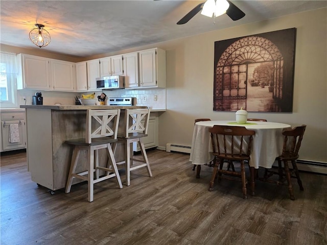 kitchen featuring a kitchen breakfast bar, white cabinetry, tasteful backsplash, stainless steel microwave, and dark wood-style flooring