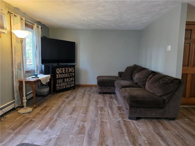 living area with a baseboard heating unit, an AC wall unit, baseboards, a textured ceiling, and wood finished floors