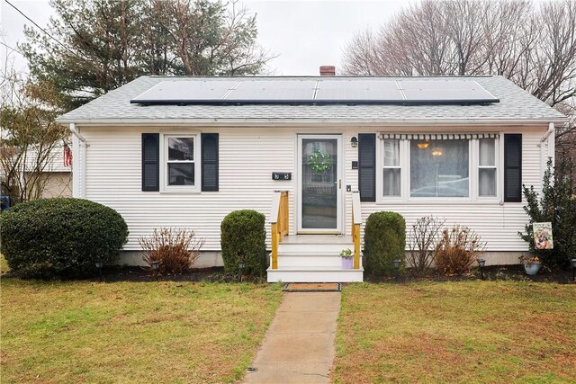 bungalow-style house with a front yard, roof with shingles, and roof mounted solar panels