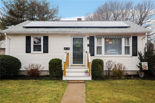 bungalow-style house featuring solar panels, roof with shingles, and a front lawn