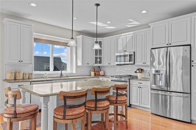 kitchen with light wood finished floors, white cabinets, a kitchen breakfast bar, and appliances with stainless steel finishes