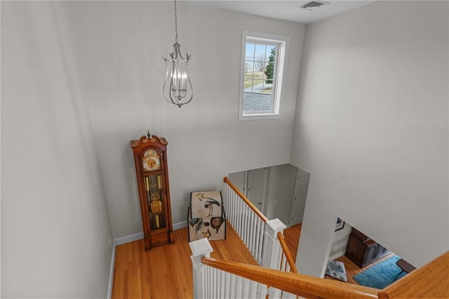 stairway with baseboards, visible vents, wood finished floors, and an inviting chandelier