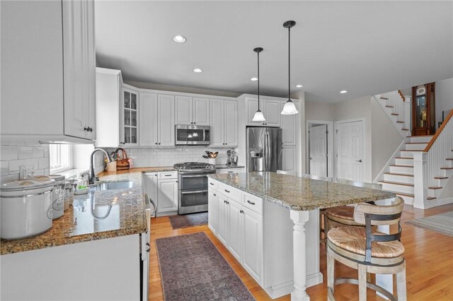 kitchen featuring white cabinetry, a breakfast bar, a sink, light wood-style floors, and appliances with stainless steel finishes
