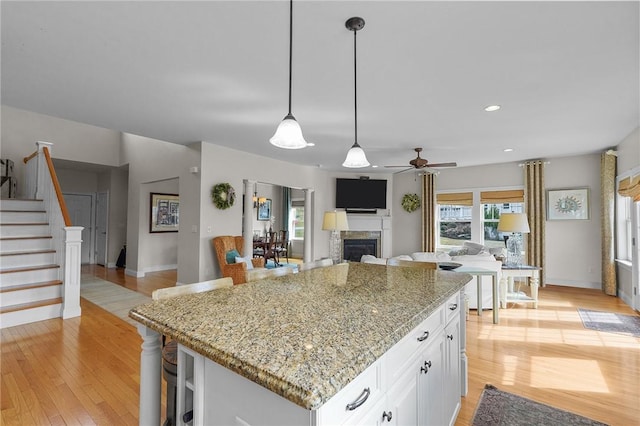 kitchen featuring white cabinetry, light wood finished floors, a fireplace, and ceiling fan