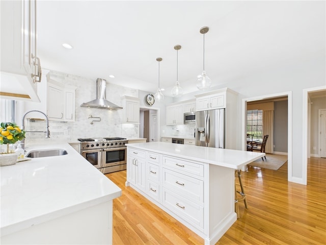 kitchen with a sink, stainless steel appliances, light wood-style floors, decorative backsplash, and wall chimney range hood