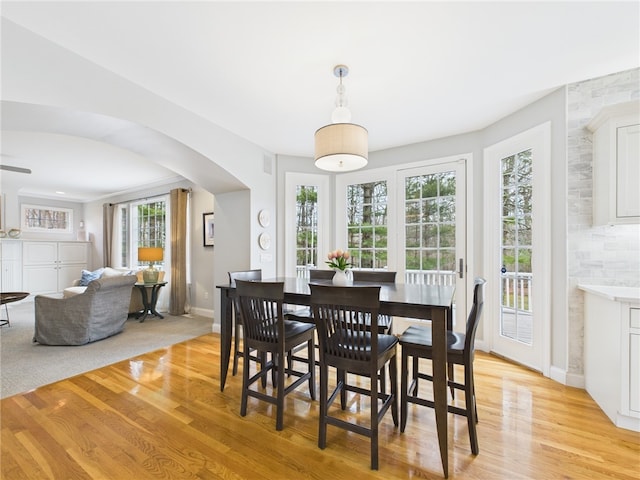 dining area featuring baseboards, light wood-style flooring, and arched walkways