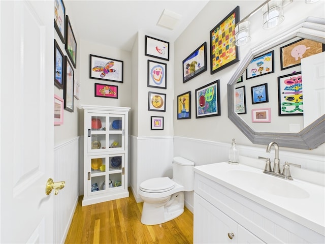 bathroom featuring wood finished floors, a wainscoted wall, toilet, and vanity