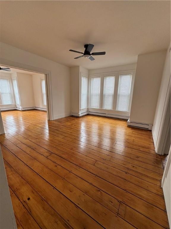 unfurnished room featuring plenty of natural light, a ceiling fan, a baseboard heating unit, and hardwood / wood-style floors
