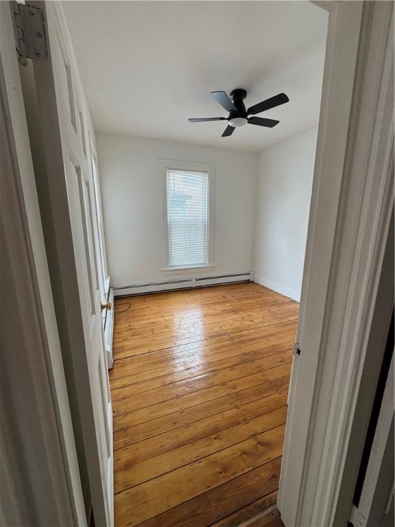 unfurnished bedroom featuring wood-type flooring, a baseboard radiator, and ceiling fan