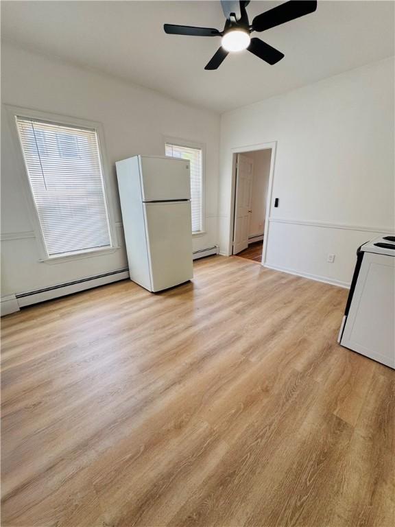 interior space with a ceiling fan, a baseboard heating unit, and light wood-style flooring