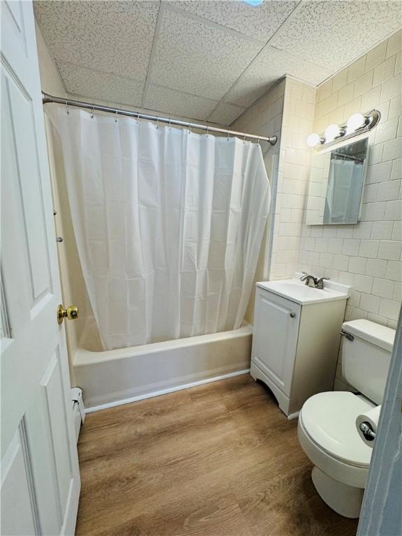 bathroom with vanity, toilet, shower / bath combination with curtain, a drop ceiling, and wood finished floors