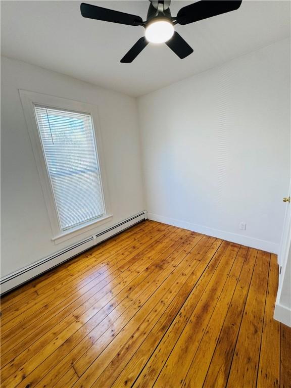 spare room with wood-type flooring, a ceiling fan, baseboards, and a baseboard heating unit
