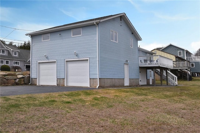 back of property featuring stairs, a deck, aphalt driveway, a lawn, and a garage