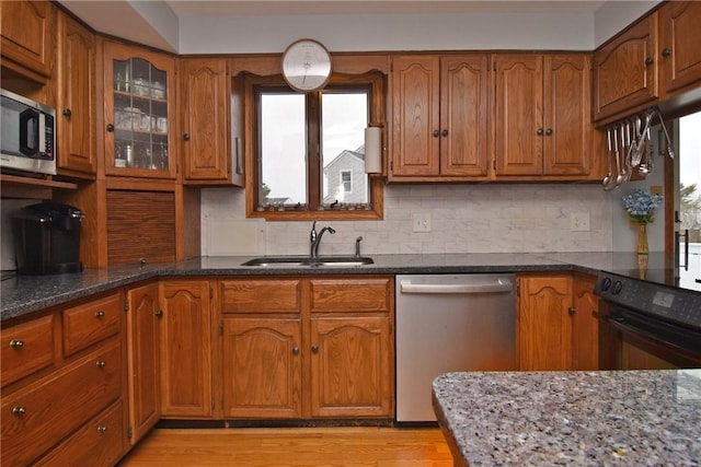 kitchen with dark stone countertops, a sink, stainless steel appliances, and brown cabinetry