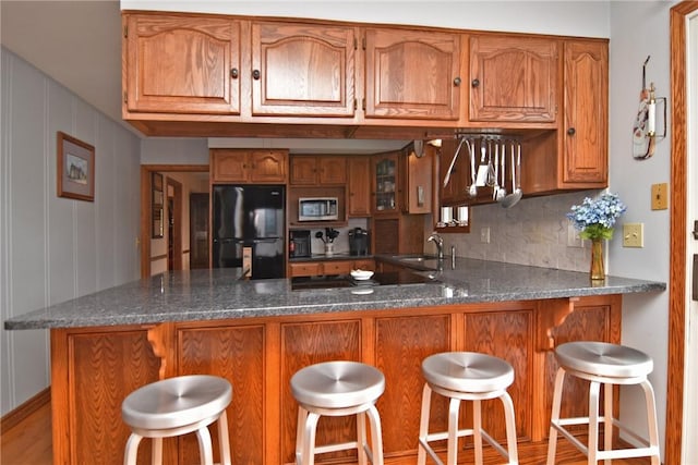 kitchen with decorative backsplash, stainless steel microwave, brown cabinetry, and freestanding refrigerator