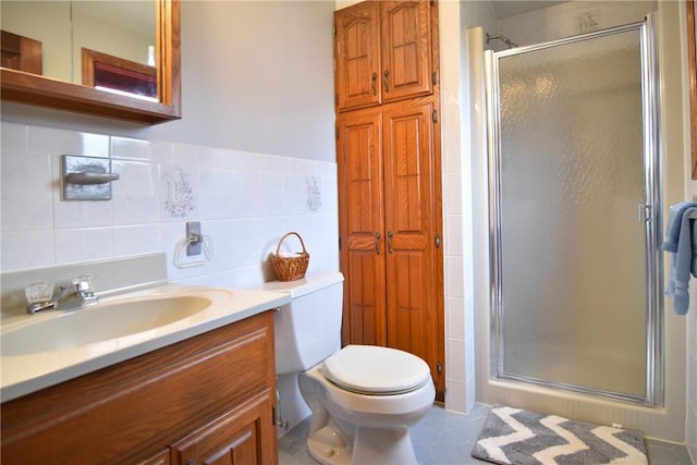 full bath with toilet, vanity, a stall shower, and tile walls