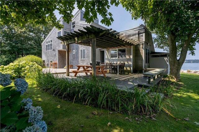 rear view of property featuring a lawn, a deck with water view, and a pergola