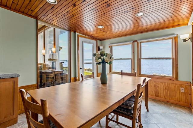 dining space featuring wooden walls, a wainscoted wall, a water view, and wood ceiling