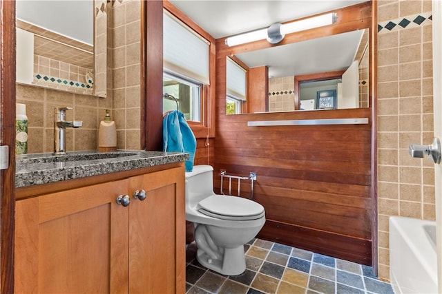 bathroom with tile walls, toilet, a bath, and vanity