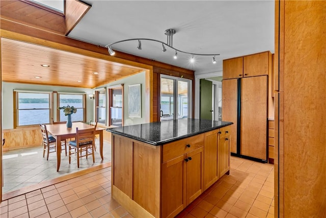 kitchen with a kitchen island, light tile patterned flooring, paneled fridge, and dark stone counters