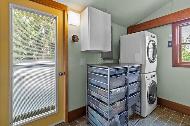 laundry room with stacked washer and dryer, cabinet space, dark tile patterned flooring, and baseboards