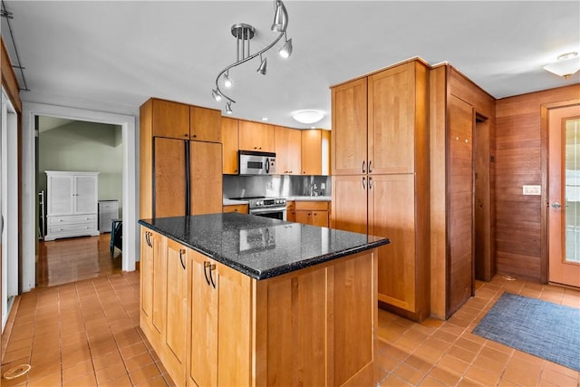 kitchen featuring dark stone counters, brown cabinets, stainless steel appliances, light tile patterned floors, and a center island