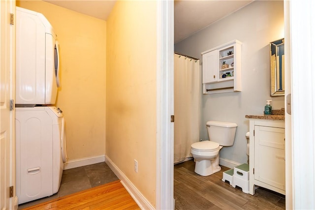 full bathroom with baseboards, wood finished floors, toilet, and stacked washer / dryer