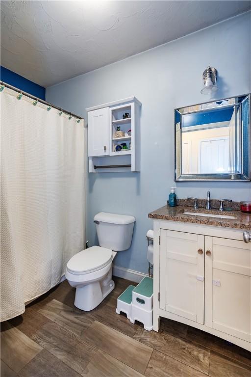 full bath featuring baseboards, wood finished floors, toilet, and vanity