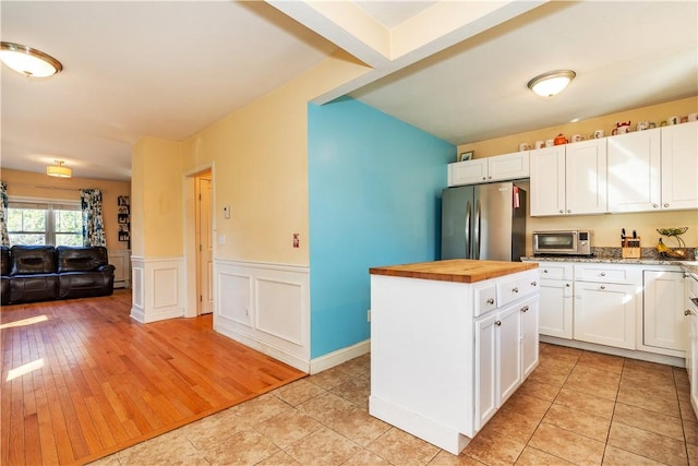 kitchen with butcher block countertops, stainless steel appliances, a kitchen island, white cabinetry, and wainscoting
