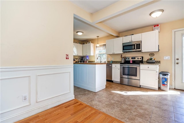 kitchen featuring a sink, white cabinetry, wainscoting, stainless steel appliances, and beamed ceiling