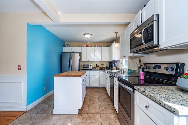 kitchen featuring a sink, a kitchen island, white cabinetry, stainless steel appliances, and wood counters
