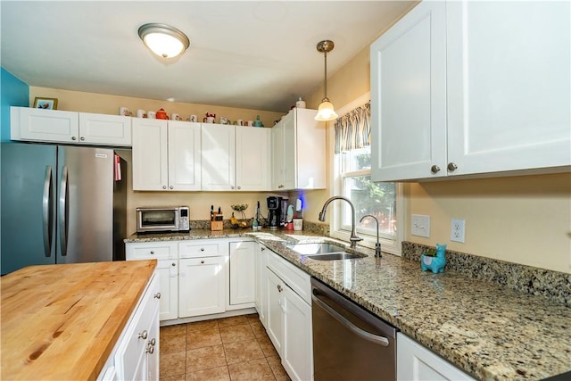 kitchen featuring butcher block countertops, stainless steel appliances, white cabinetry, a sink, and pendant lighting