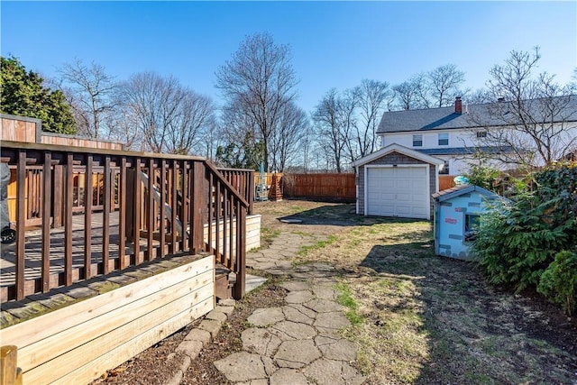 view of yard featuring fence, a detached garage, a deck, driveway, and an outbuilding