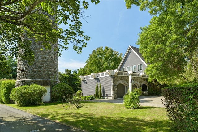 view of front of house featuring a front lawn, a balcony, driveway, and stone siding