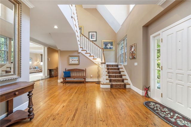 foyer entrance featuring baseboards, high vaulted ceiling, wood finished floors, and stairway