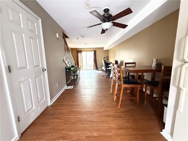 dining room featuring stairs, baseboards, visible vents, a ceiling fan, and wood finished floors