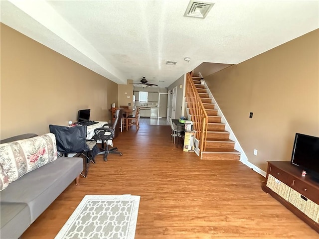 living area with stairs, a textured ceiling, light wood-style floors, visible vents, and a ceiling fan