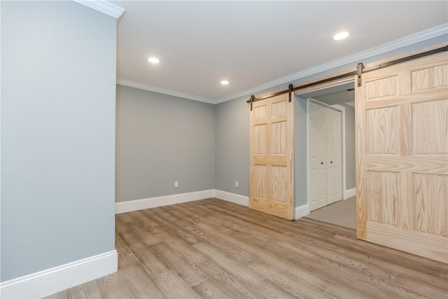 unfurnished bedroom featuring crown molding, a barn door, recessed lighting, baseboards, and wood finished floors